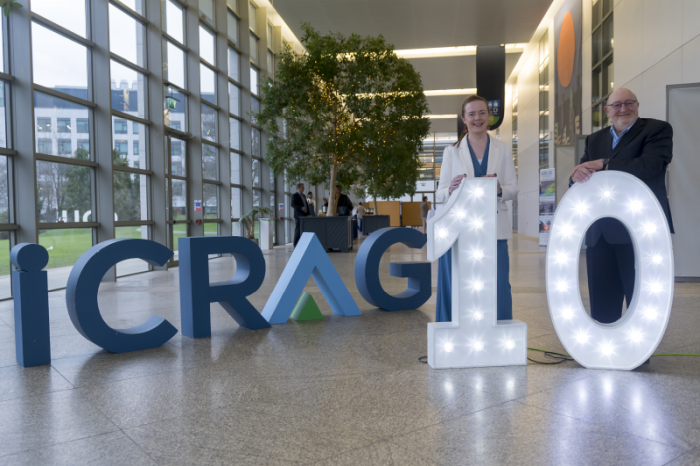 Two people standing in front of a lit up 10 and the letters iCRAG in the background